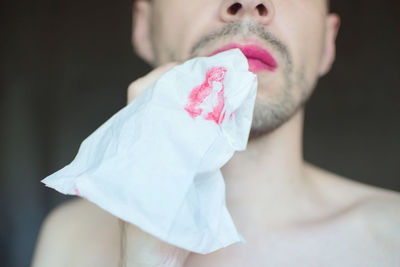 Midsection of transgender man carrying tissue paper with lipstick in mouth