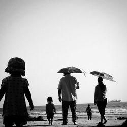 Rear view of family walking on shore against clear sky