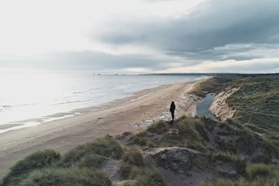 Rear view of woman standing on beach against sky
