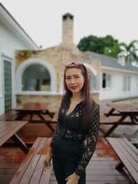 Portrait of woman smiling while standing against built structure during rainy season