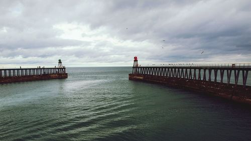 Piers in sea against cloudy sky