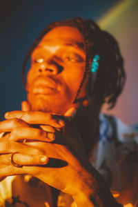 Serious african american male with braided hairstyle and chain looking away on dark background in studio with dim light