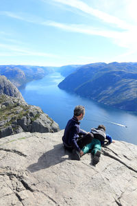 Man sitting on rock by mountain against sky