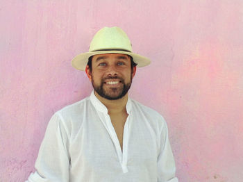 Portrait of man wearing hat standing against pink wall