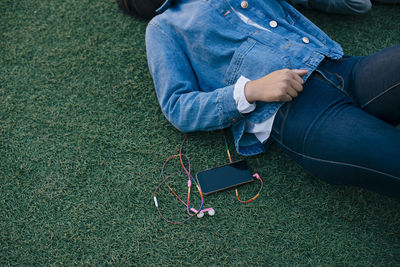 Midsection of teenage girl lying by mobile phone on grass