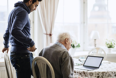 Caretaker and senior male using laptop at dinning table