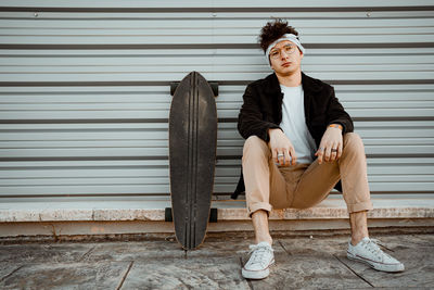 Young man looking away while sitting on shutter