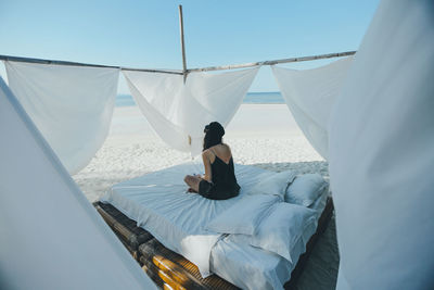 Rear view of woman sitting on bed at beach