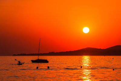 Silhouette sailboats in sea against orange sky