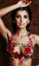 Portrait of shirtless young woman with floral decoration standing against wall