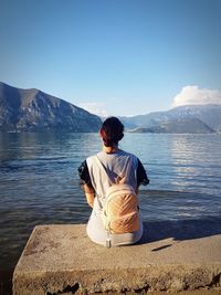 Rear view of woman sitting by lake against mountain