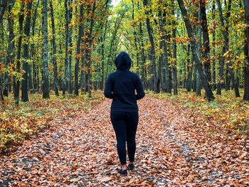 Back of woman wearing black tracksuit with hoodie standing alone in the middle of the forest