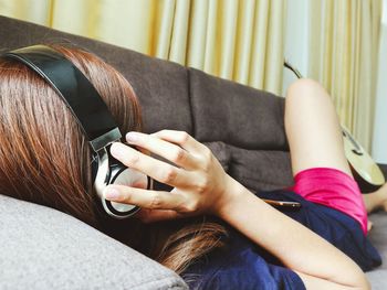 Woman wearing headphones while lying on sofa at home
