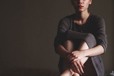 Midsection of woman sitting against gray background