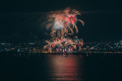 Firework display over illuminated city against clear sky at night