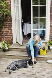 Senior woman stroking dog lying at house entrance