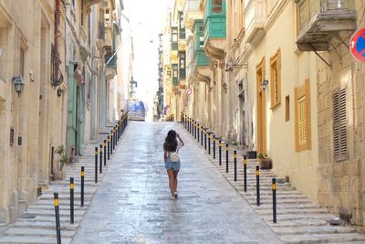 Rear view of woman walking on alley amidst buildings in city