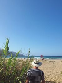 Rear view of man standing on beach against clear blue sky