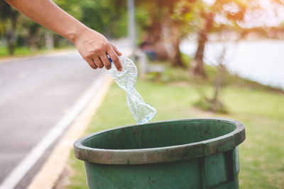 Cropped hand throwing bottle in garbage can