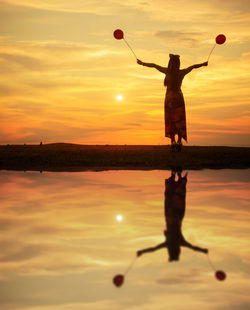 Reflection of woman with balloons standing in sea against sky