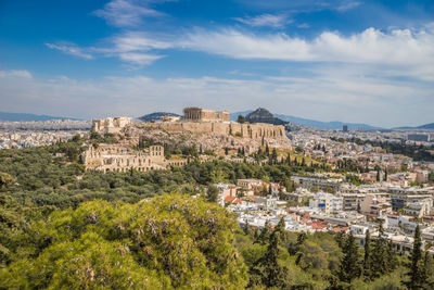 Aerial view of buildings against cloudy sky in city during sunny day