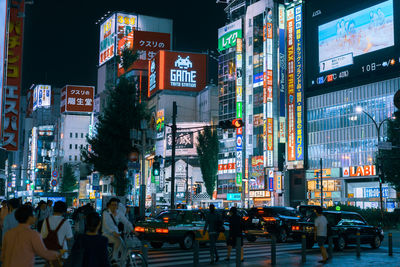 People on illuminated street amidst buildings in city at night