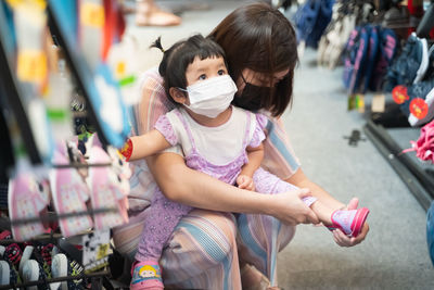 Mother wearing mask putting shoes on of daughter at market