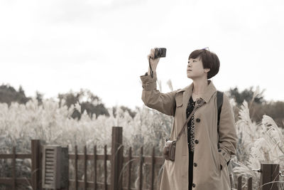 Woman photographing while standing against sky