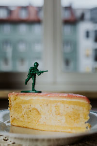 Toy soldier standing on the top of a piece of cake - close up of figurine aginst window background