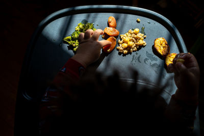 High angle view of a toddler's hands exploring a tray of brightly colored foods during mealtime