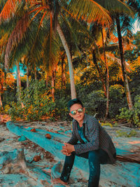 Portrait of young man sitting on plant against trees