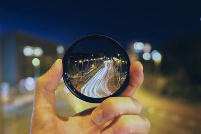 Close-up of hand holding lens against road at night