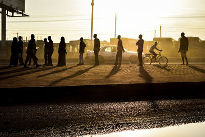 Sunrise silhouette scene of people standing and a man in a bicycle and a car