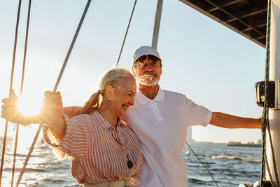 Smiling couple standing on boat in sea against sky