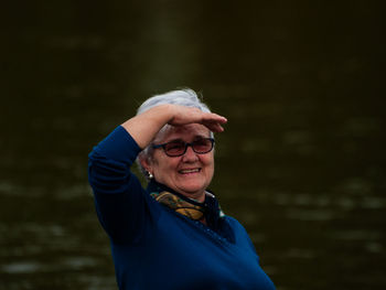 Portrait of smiling woman shielding eyes while standing against river