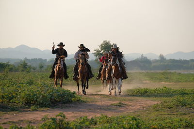 People riding horse on field against sky