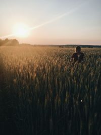 Girl standing amidst plants against sky during sunset