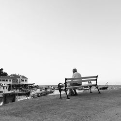 Rear view of man sitting on floor against clear sky