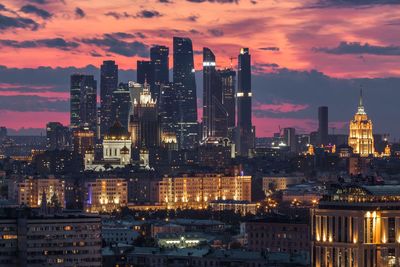 Illuminated buildings in city against sky at sunset