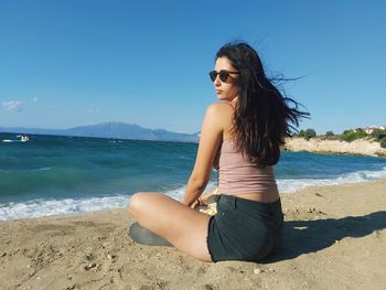 Young woman sitting at beach on sunny day