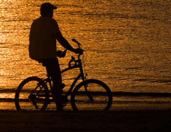 Silhouette man riding bicycle at beach during sunset