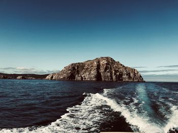 Scenic view of rocks in sea against clear blue sky