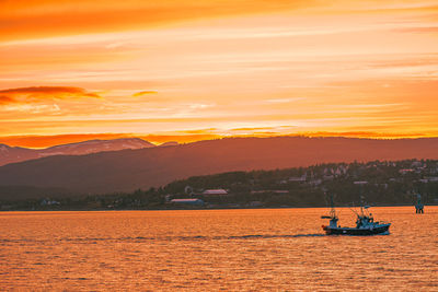 Boat sailing on sea against orange sky