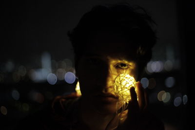 Close-up portrait of teenage boy holding illuminated light at night