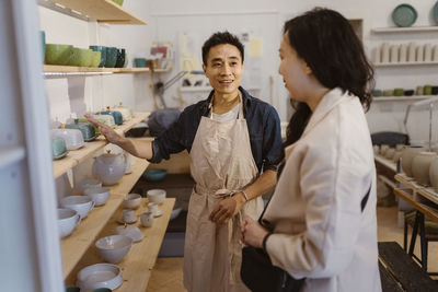 Craftsman assisting female customer while buying ceramics at workshop