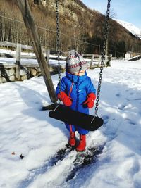 Full length of child standing by swing on snow covered field