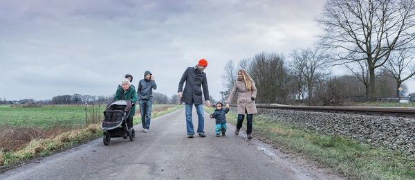 Family walking on dirt road against sky during winter