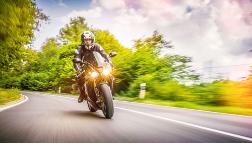 Blurred motion of man riding motorcycle on road against cloudy sky