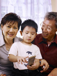 Boy holding remote control while sitting with grandparents at home