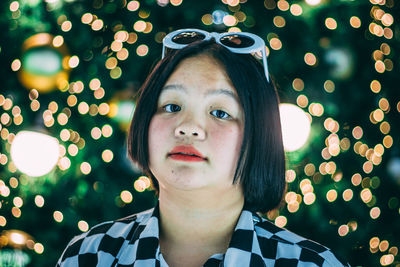 Close-up portrait of woman against illuminated lighting equipment at night